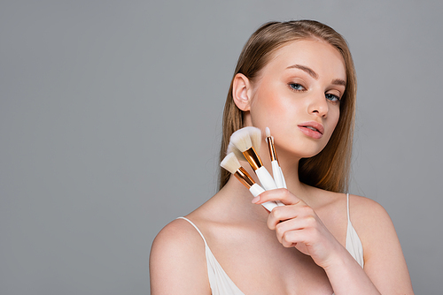pretty young woman holding set of different cosmetic brushes isolated on grey