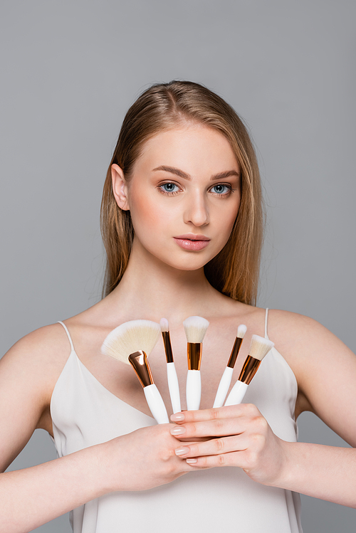 young woman holding different cosmetic brushes isolated on grey