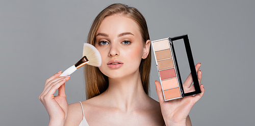 young woman holding cosmetic brush and blush palette isolated on grey, banner
