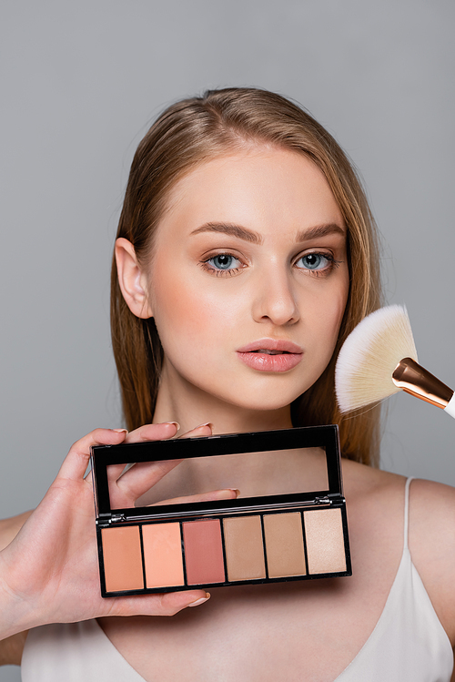 pretty woman holding cosmetic brush and blush palette isolated on grey