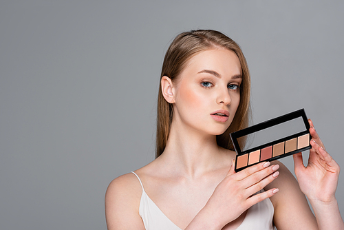 pretty young woman holding cosmetic palette isolated on grey