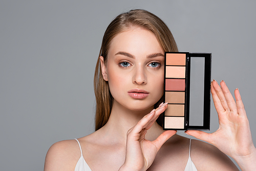 young pretty woman holding cosmetic blush palette isolated on grey