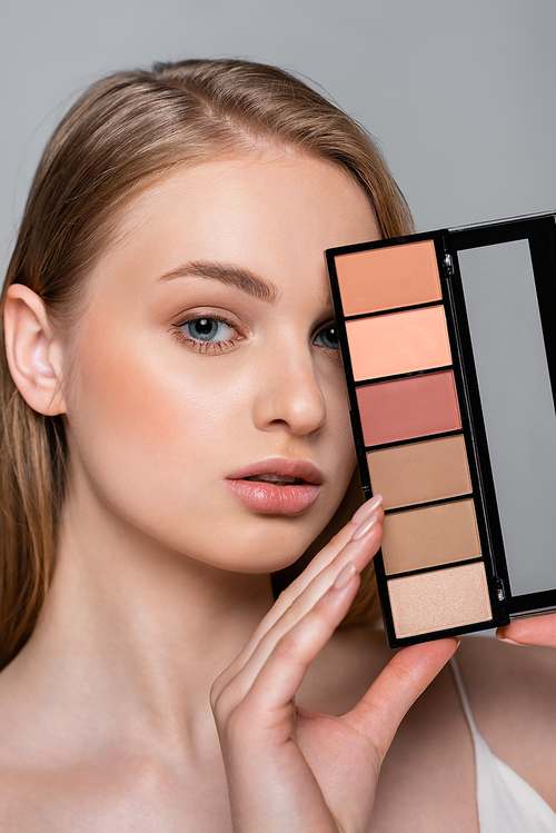 young pretty woman holding cosmetic palette isolated on grey
