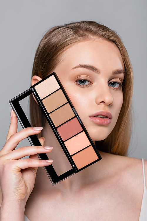 young woman holding cosmetic blush palette isolated on grey