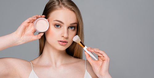 young woman holding cosmetic brush and face powder isolated on grey, banner