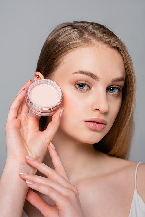 young woman holding container with face powder isolated on grey