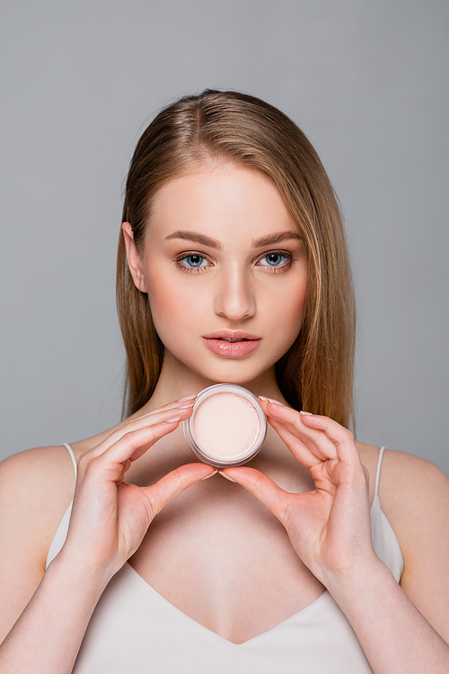pretty young woman holding container with face powder isolated on grey