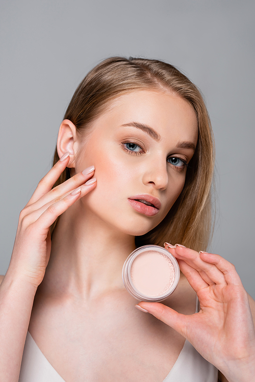 pretty blonde woman holding container with face powder isolated on grey