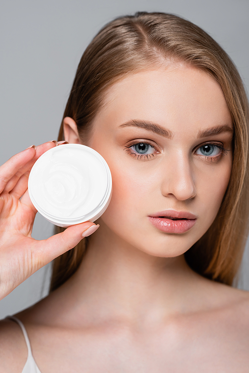 pretty young woman holding container with face cream isolated on grey