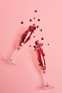 top view of champagne glasses with red confetti hearts on pink