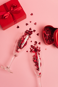 top view of champagne glasses with confetti hearts near metallic heart-shaped box and present on pink