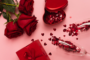 top view of champagne glasses with confetti hearts near gift boxes and roses on pink