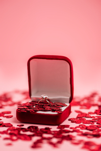 close up of jewelry box with diamond ring near shiny confetti hearts on pink