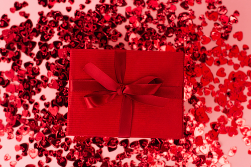 top view of wrapped present near shiny red confetti hearts on pink