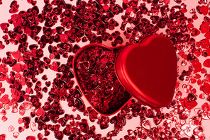 top view of metallic heart-shaped box near shiny red confetti hearts on pink