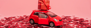 toy car with wrapped present near shiny red confetti hearts isolated on pink, banner