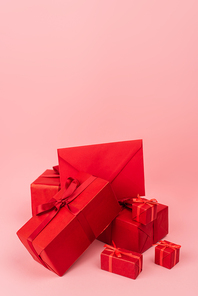 red wrapped gift boxes with ribbons and envelope on pink