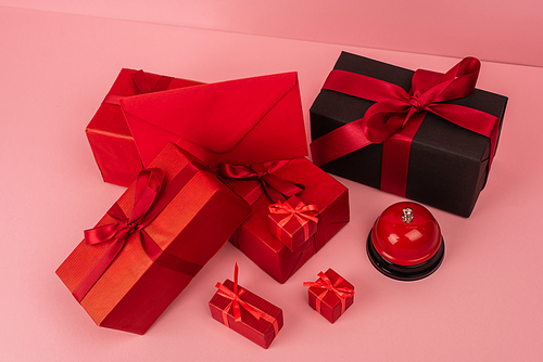 high angle view of red wrapped gift boxes and envelope near metallic bell on pink