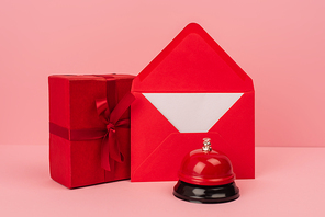 wrapped gift box and red envelope with letter near metallic bell on pink