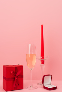 glass of champagne near gift box, engagement ring and candle on pink