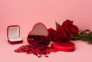 metallic heart-shaped box with confetti near red roses and engagement ring on pink