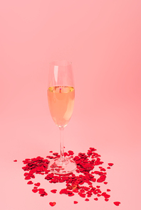 glass of champagne near red heart-shaped confetti on pink