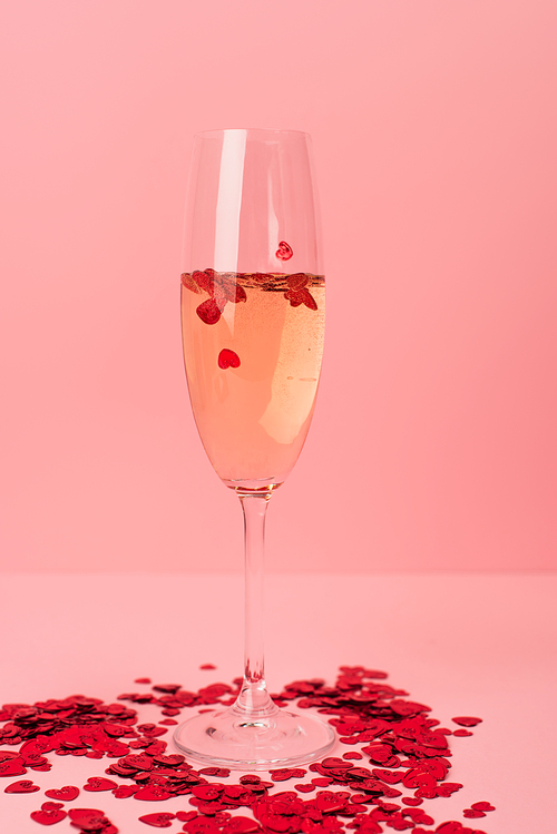 glass of champagne with red heart-shaped confetti on pink