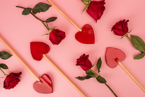 flat lay of heart-shaped lollipops near red roses on pink
