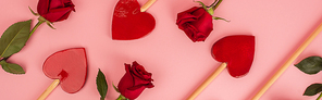 flat lay of heart-shaped lollipops near red roses on pink banner