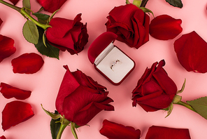 flat lay of red rose petals around jewelry box with diamond ring on pink