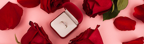 flat lay of red rose petals around jewelry box with diamond ring on pink, banner