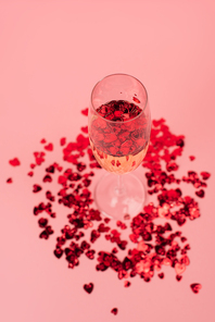 high angle view of glass with champagne and red heart-shaped confetti on pink