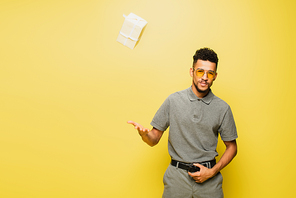 african american man in sunglasses and grey tennis shirt throwing wrapped present on yellow