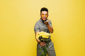 african american man in sunglasses holding bouquet of flowers and sending  isolated on yellow