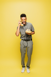 full length of happy african american man in sunglasses and grey tennis shirt talking on retro telephone on yellow