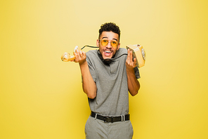 confused african american man in sunglasses and grey tennis shirt holding retro telephone on yellow