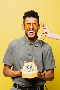 woman holding handset near african american man in sunglasses and grey tennis shirt on yellow