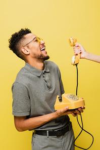 woman holding handset near positive african american man in sunglasses and grey tennis shirt isolated on yellow