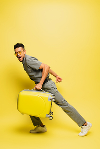 full length of amazed african american man in sunglasses and grey tennis shirt with luggage on yellow