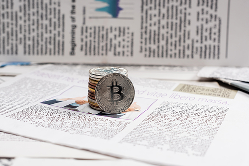 KYIV, UKRAINE - NOVEMBER 1, 2021: metallic bitcoins on printed newspaper