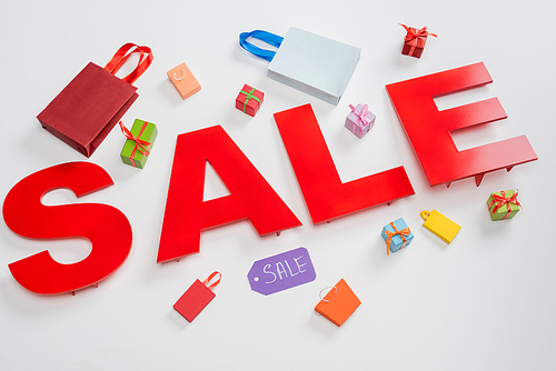 high angle view of sale letters near tiny shopping bags and presents on white