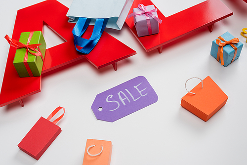 high angle view of sale tag near tiny shopping bags and presents on white