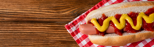 top view of tasty hot dog with sauces on checkered napkin and wooden table, banner