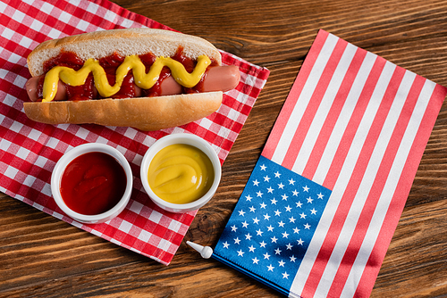 top view of hot dog, ketchup and mustard near small usa flag on wooden table