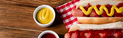 top view of sauce bowls near hot dogs and plaid napkin on wooden table, banner