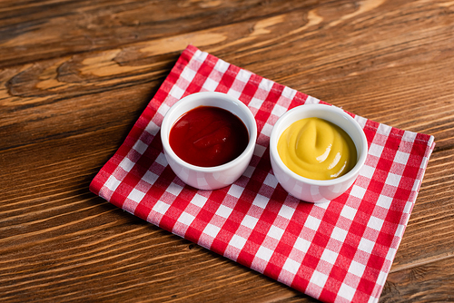 sauce bowls with ketchup and mustard on checkered napkin and wooden table