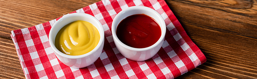 bowls with ketchup and mustard on checkered napkin and wooden table, banner