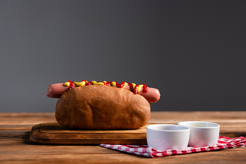 sauce bowls and plaid napkin near tasty hot dogs on wooden table isolated on grey