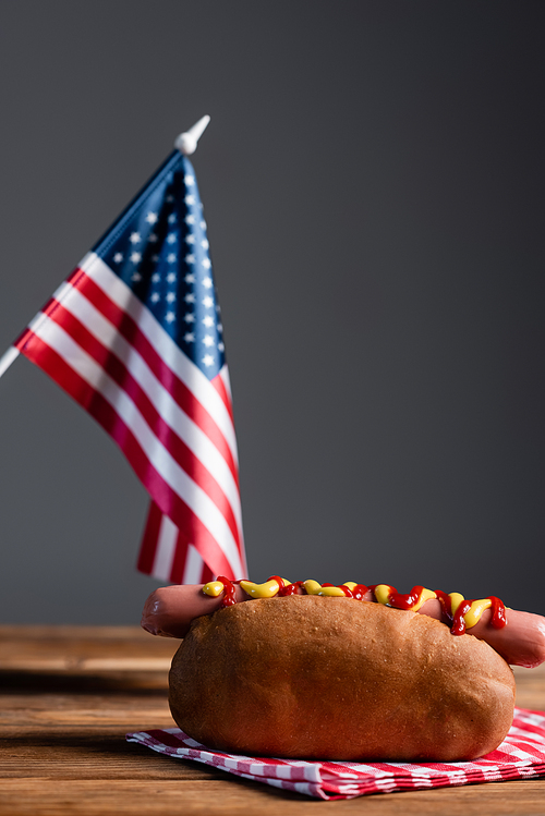 blurred american flag, hot dog and plaid napkin on wooden table isolated on grey