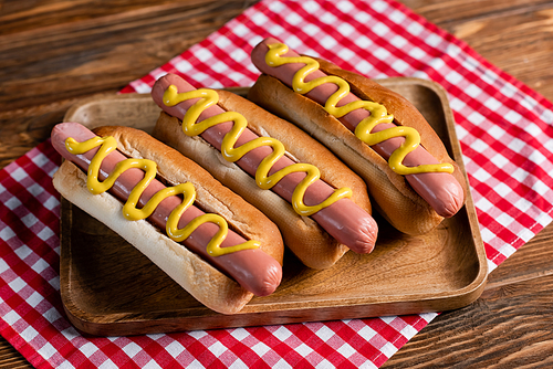 wooden tray with tasty hot dogs and checkered napkin on wooden table